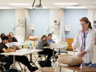 Photo of students watching professor use dummy as an example during a simulation. 