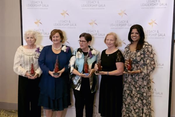 5 women standing together each holding a red glass trophy  