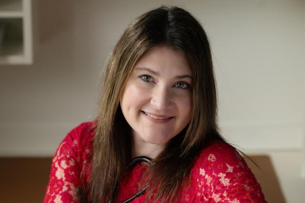 Headshot photo of Lauren Cole, Sitting on a chair turned with her arms over the back of the chair, smiling. 