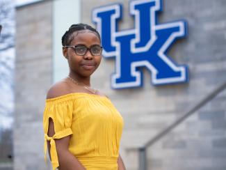 Student standing in front of UK sign on building.