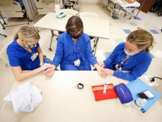 Two students practicing finding a vein for an IV on a professor.