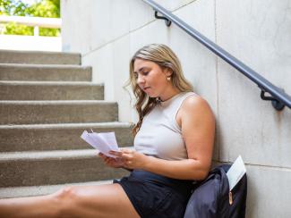 Student sitting on steps holding papers