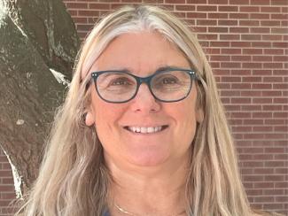 woman with long light colored hair wearing a black shirt in front of a brick wall