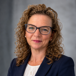 A headshot photo of Carla Orsburn. She is wearing glasses and a navy blazer and smiling. 