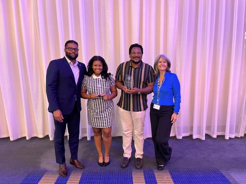 Photo of Corey Moore, Jordan Brown, Omar Brown, and Lee Anne Walmsley smiling. Jordan and Omar are holding awards. 