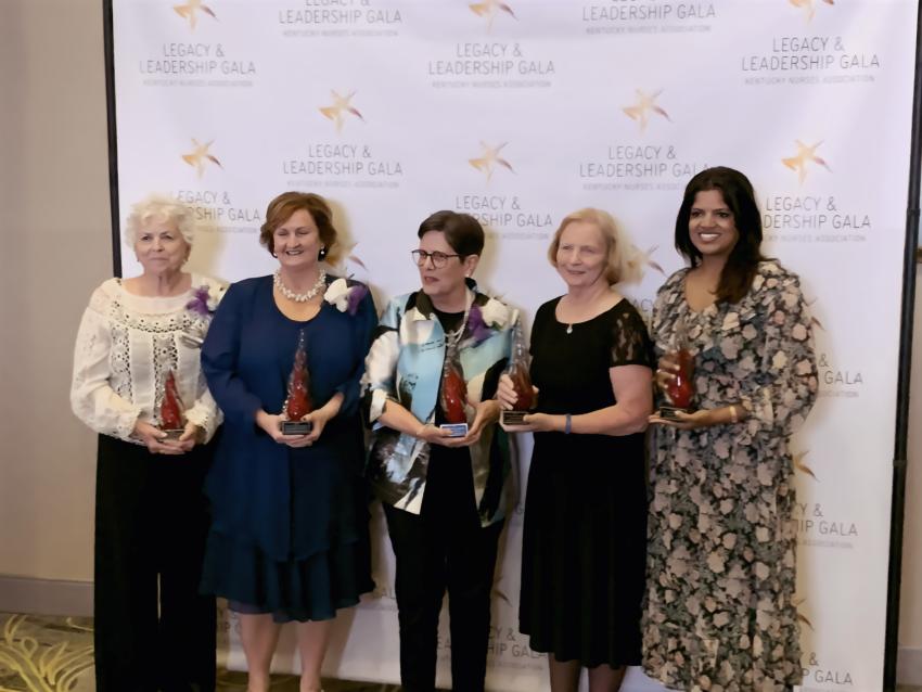 5 women standing together each holding a red glass trophy