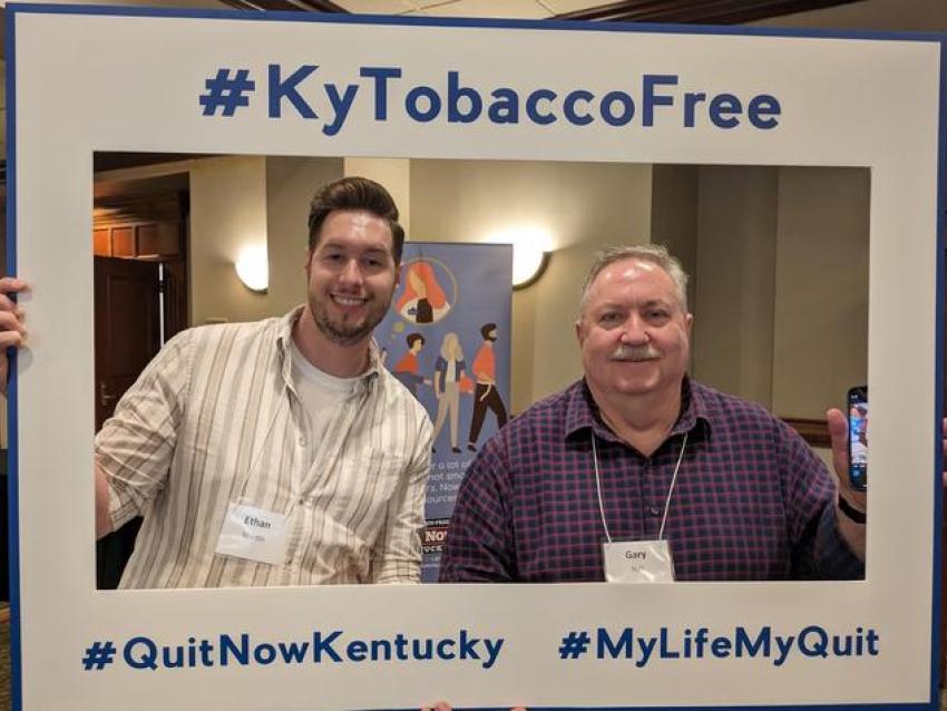 Two men smiling in a frame cutout that says "#KyTobaccoFree #QuitNowKentucky #MyLifeMyQuit"