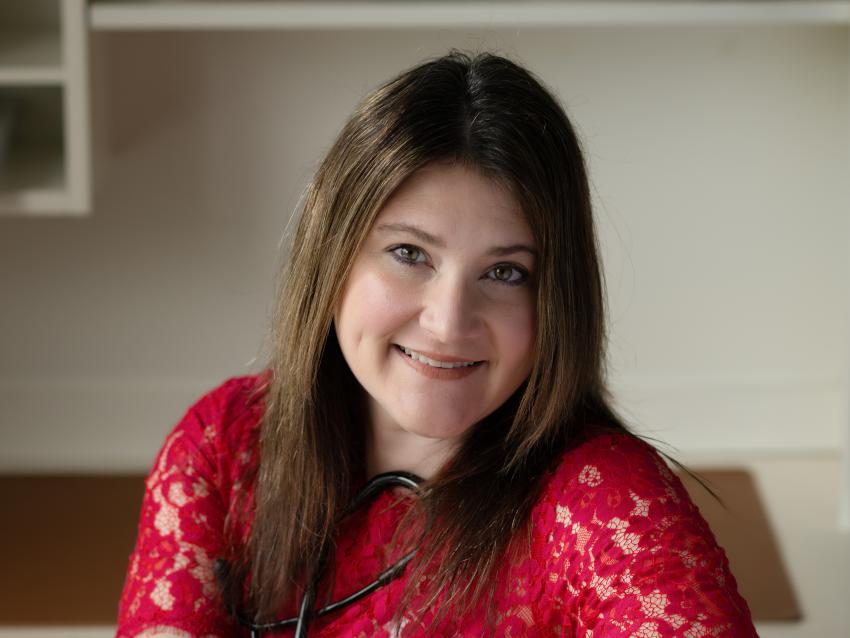 Headshot photo of Lauren Cole, Sitting on a chair turned with her arms over the back of the chair, smiling. 