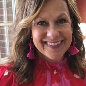 Woman with long light brown hair wearing a red and pink shirt smiling