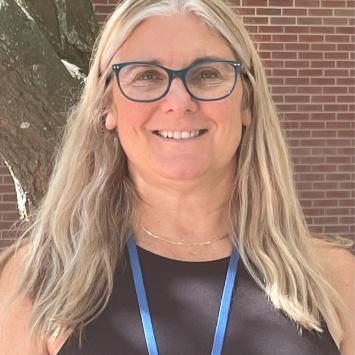 woman with long light colored hair wearing a black shirt in front of a brick wall