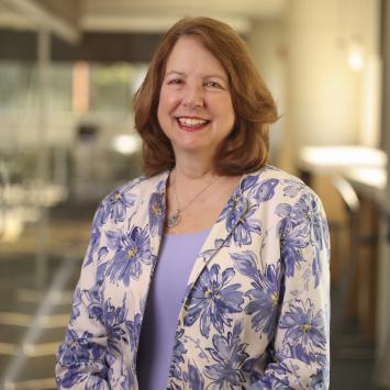 Woman with brown hair wearing a purple floral blazer smiling for a headshot.