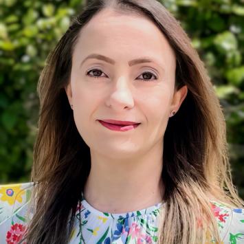 Head shot of a woman with long midtone brown hair wearing a floral shirt standing outside 