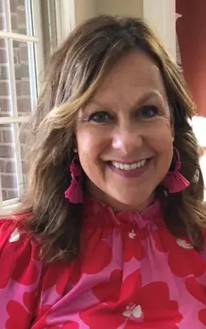 Woman with long light brown hair wearing a red and pink shirt smiling