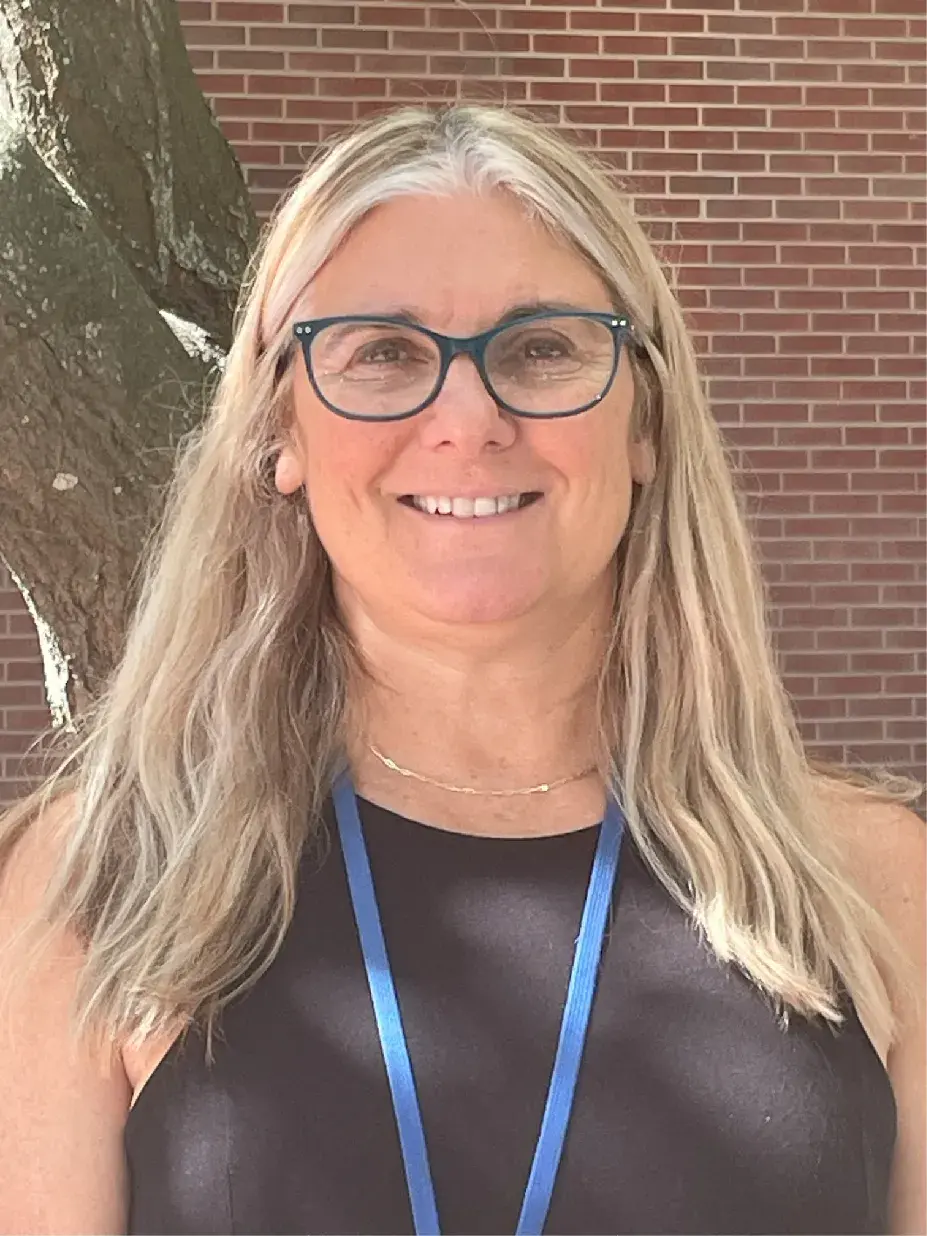 woman with long light colored hair wearing a black shirt in front of a brick wall