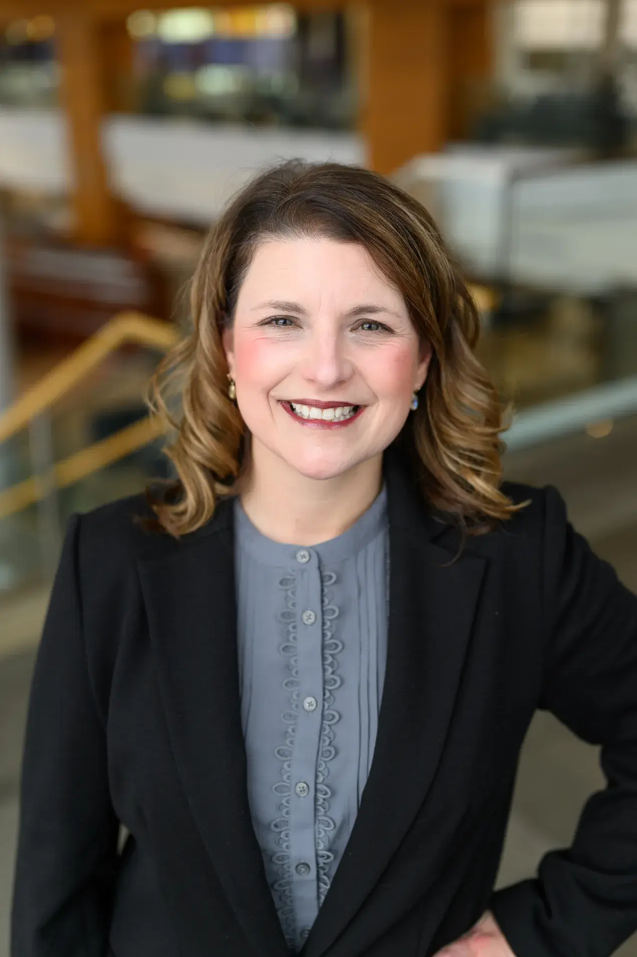 Woman in Black jacket with grey shirt smiling in front of blurred background