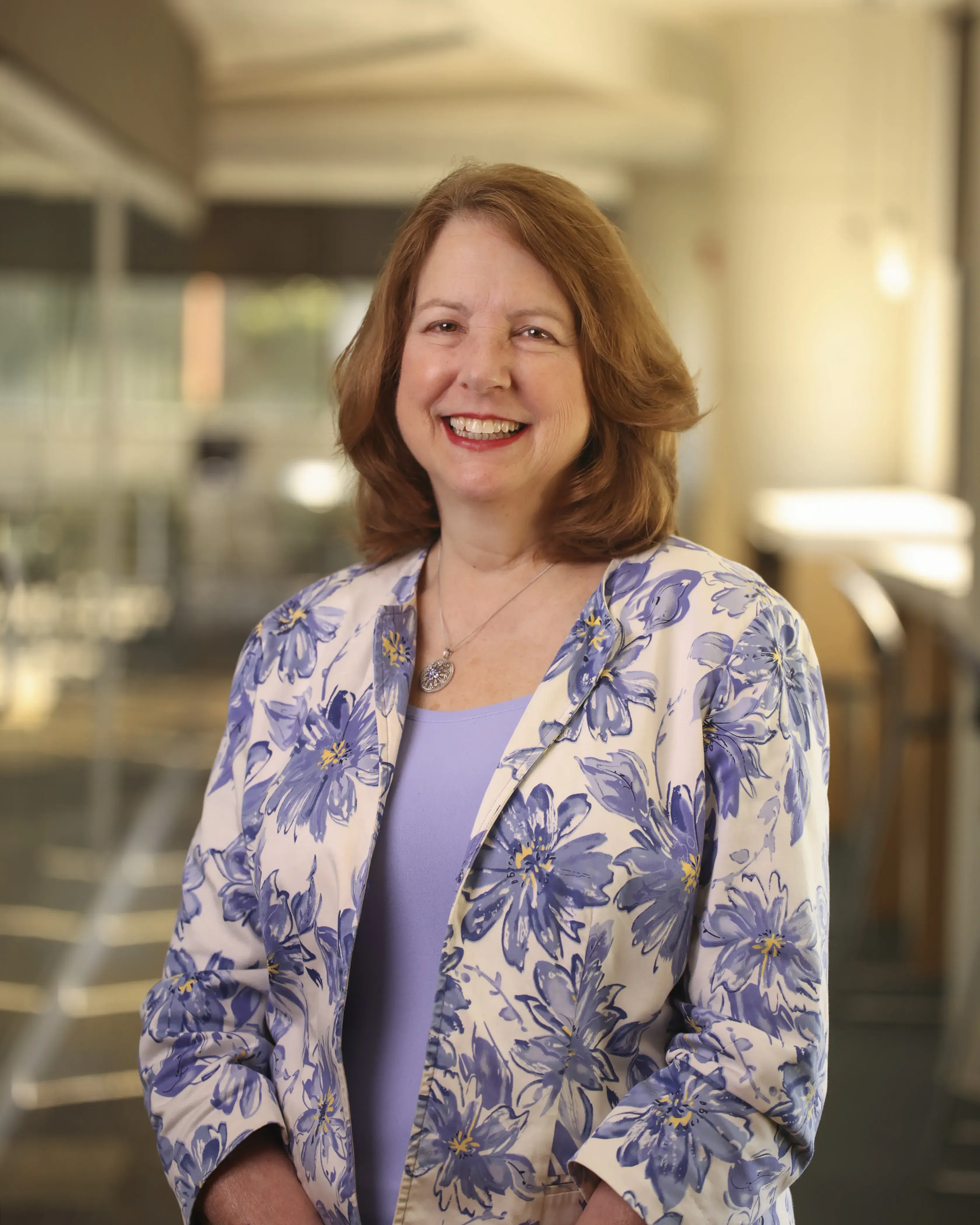Woman with brown hair wearing a purple floral blazer smiling for a headshot.