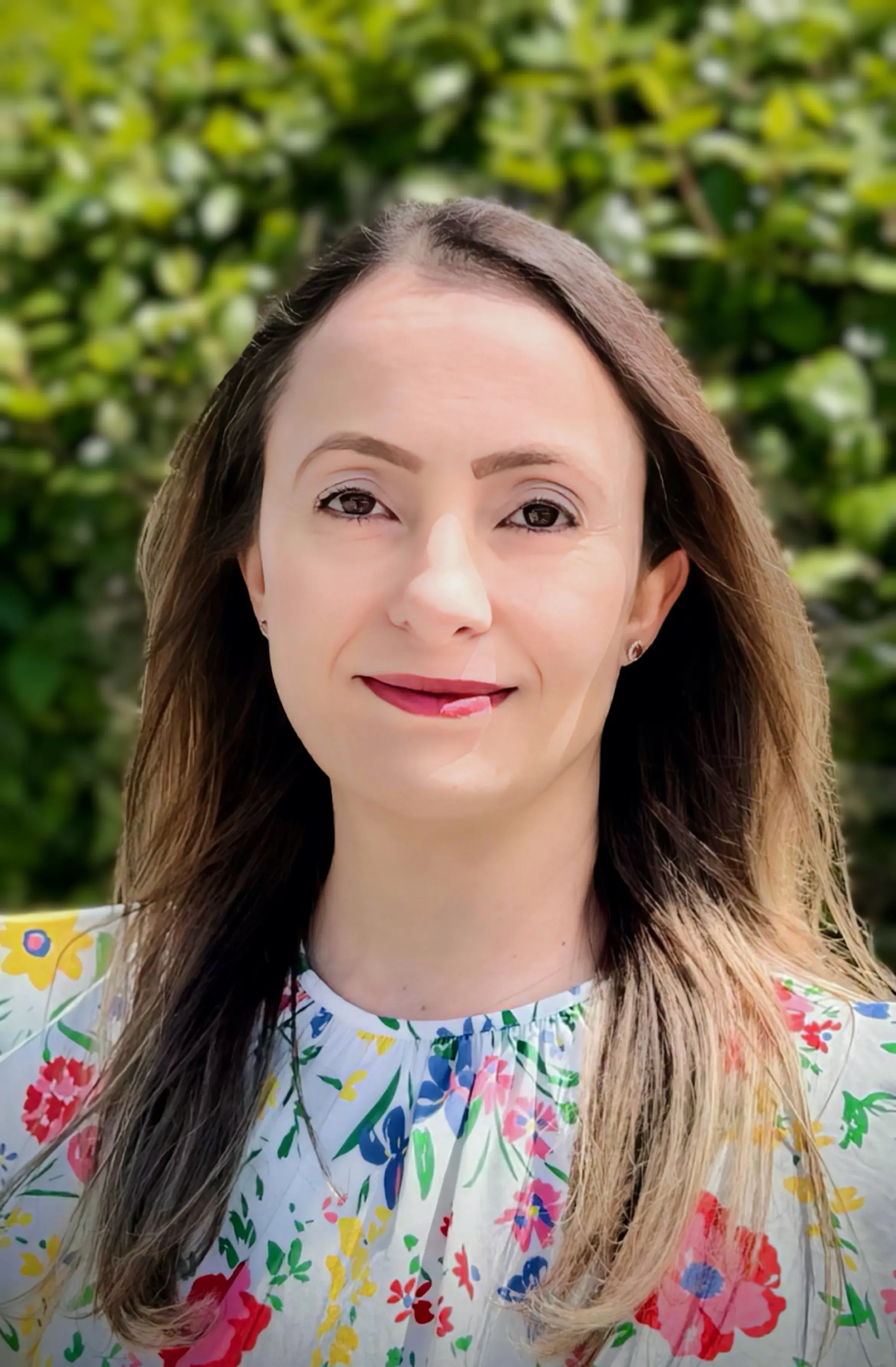 Head shot of a woman with long midtone brown hair wearing a floral shirt standing outside 