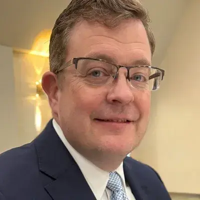 Headshot of a man with a navy suit on and glasses smiling 